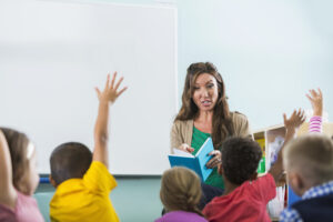 Teacher reading to students who have hands raised