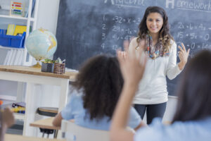 Teacher in front of classroom and student raising hand