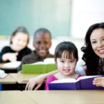 dark haired teacher next to students who are reading