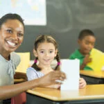 Black elementary teacher smiling at camera with little girl