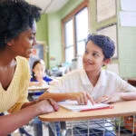 A young teacher assisting a student with classwork at his desk