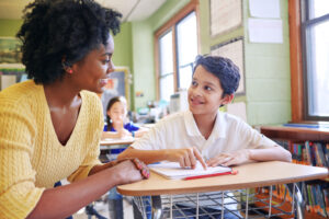 A young teacher assisting a student with classwork at his desk