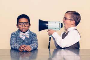 A young boy nerd shouts at the top of his voice to his co-worker through a megaphone trying to talk some sense into him but he is not listening and is ignoring him. The young nerds are dressed in bowties and glasses. Retro styling.