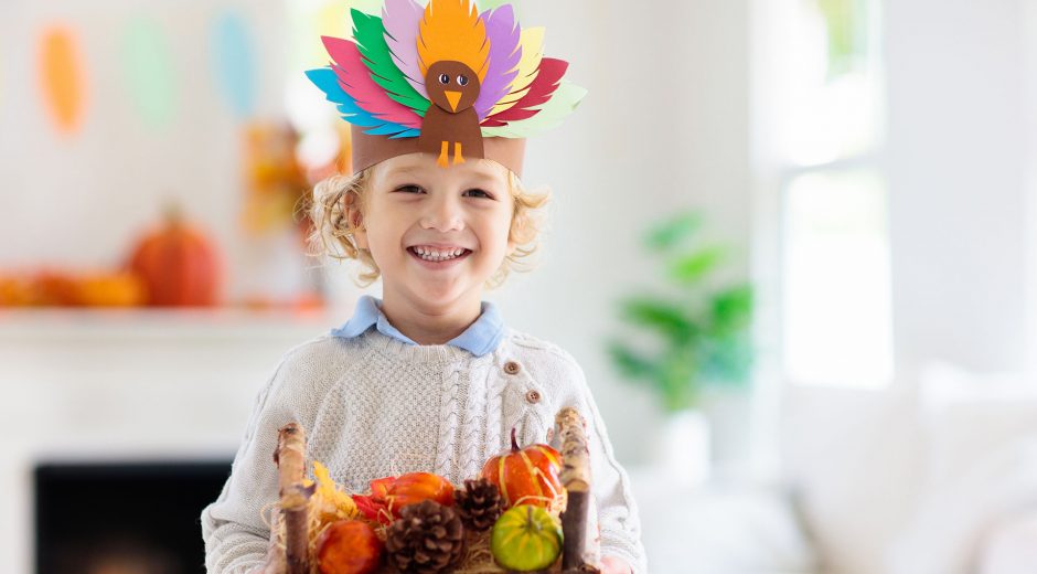 Child celebrating Thanksgiving. Kid holding pumpkin in paper turkey hat. Autumn fun crafts and art. Little blond curly boy in decorated living room. Warm knitted wear. Fall season decoration.