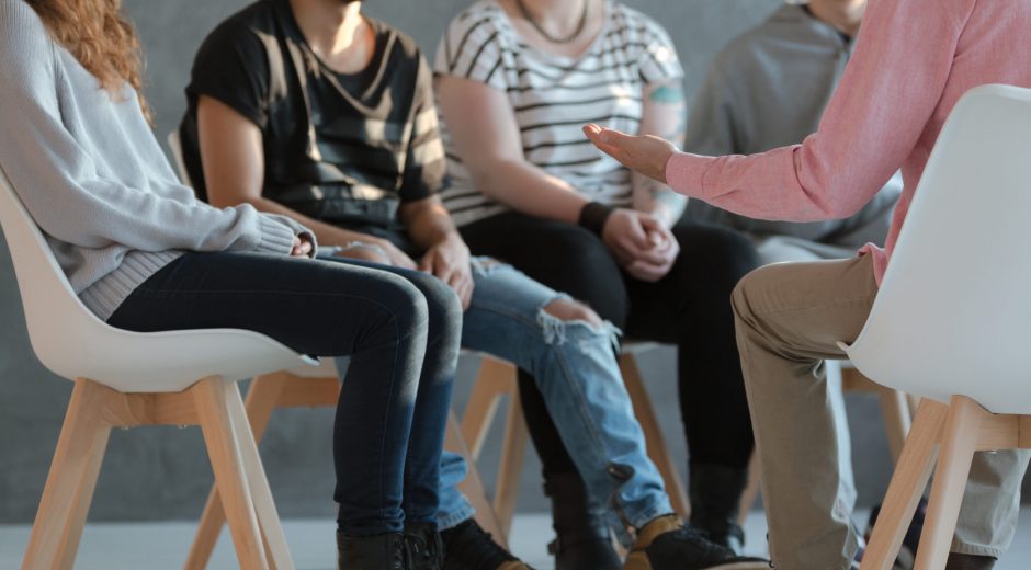 Group of young people sitting in a circle and talking to psychiatrist  during a therapy