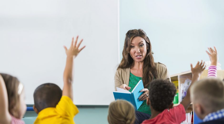 Teacher reading to students who have hands raised