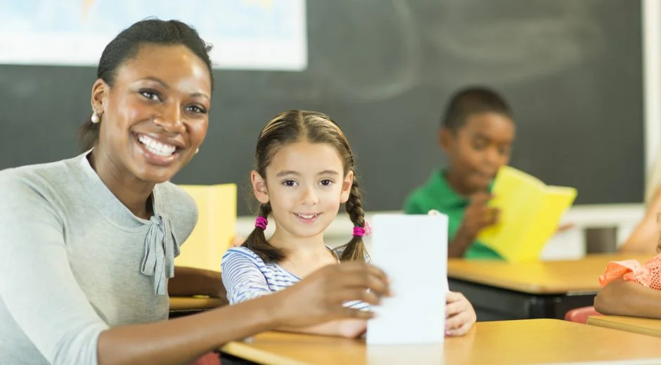 Black elementary teacher smiling at camera with little girl