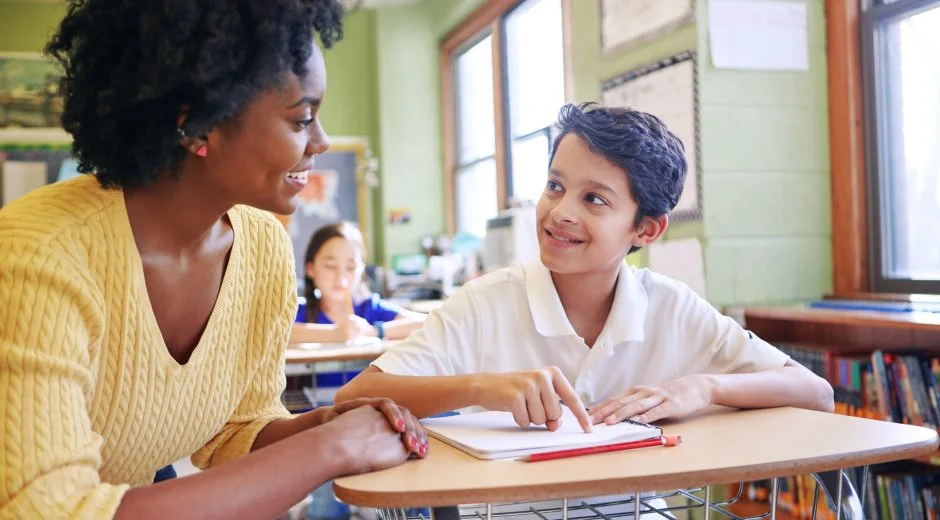 A young teacher assisting a student with classwork at his desk