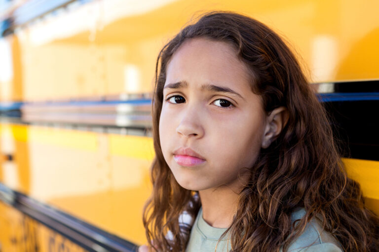sad girl next to a school bus