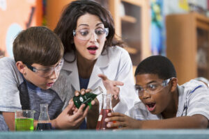 Hispanic teacher (20s) in science lab with multi-ethnic elementary school students, doing chemistry experiment.