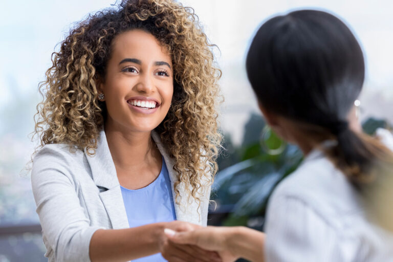 Attractive young mixed race businesswoman shakes hands with a female colleague during a teacher interview at a job fair.